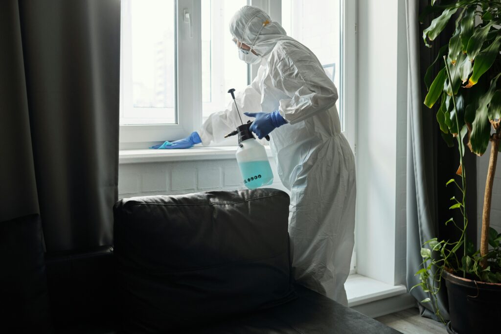 Person in PPE disinfecting indoor window area during COVID-19 pandemic.