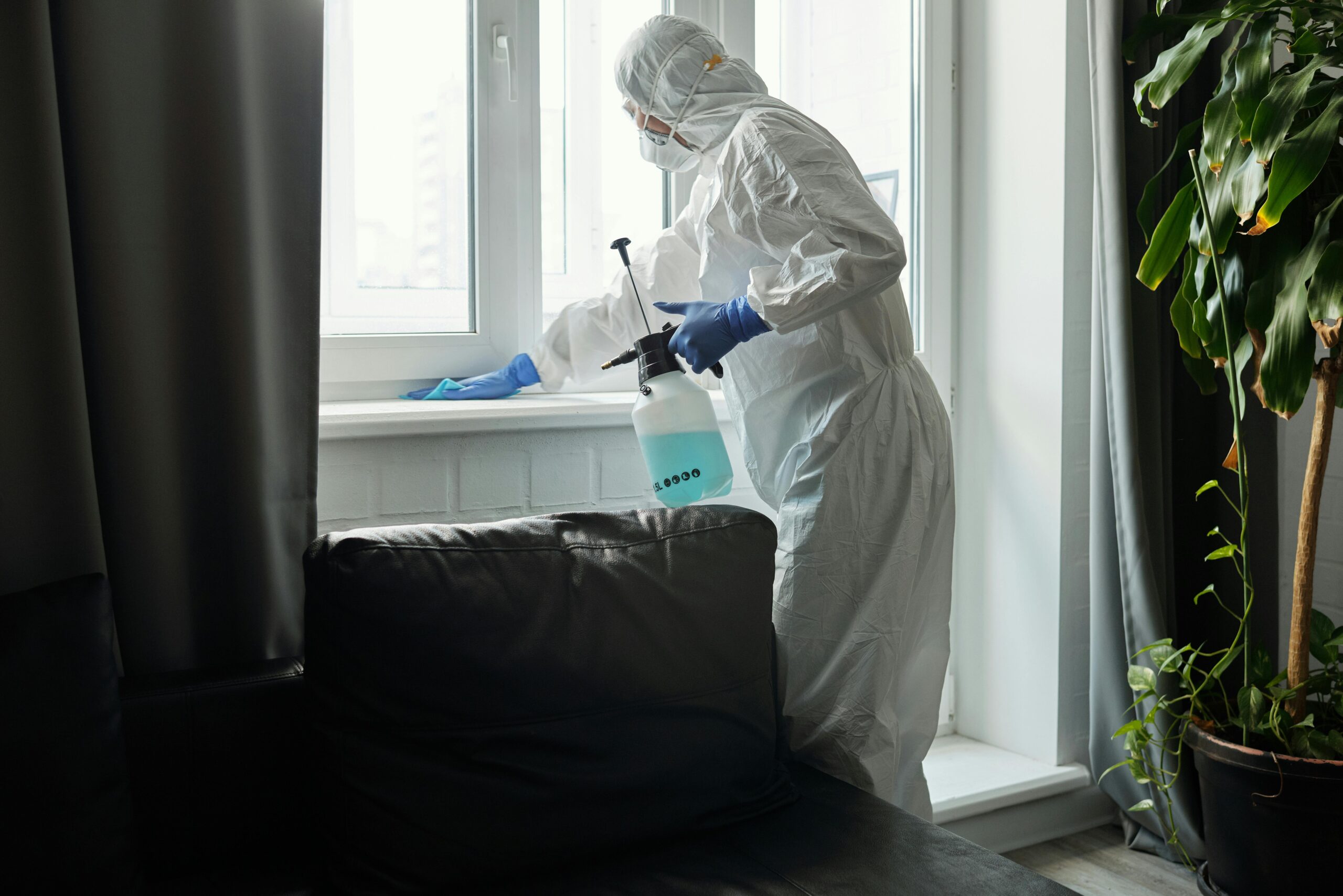 Person in PPE disinfecting indoor window area during COVID-19 pandemic.