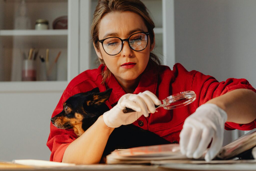 A woman wearing glasses examines documents with a magnifying glass, holding her dog.